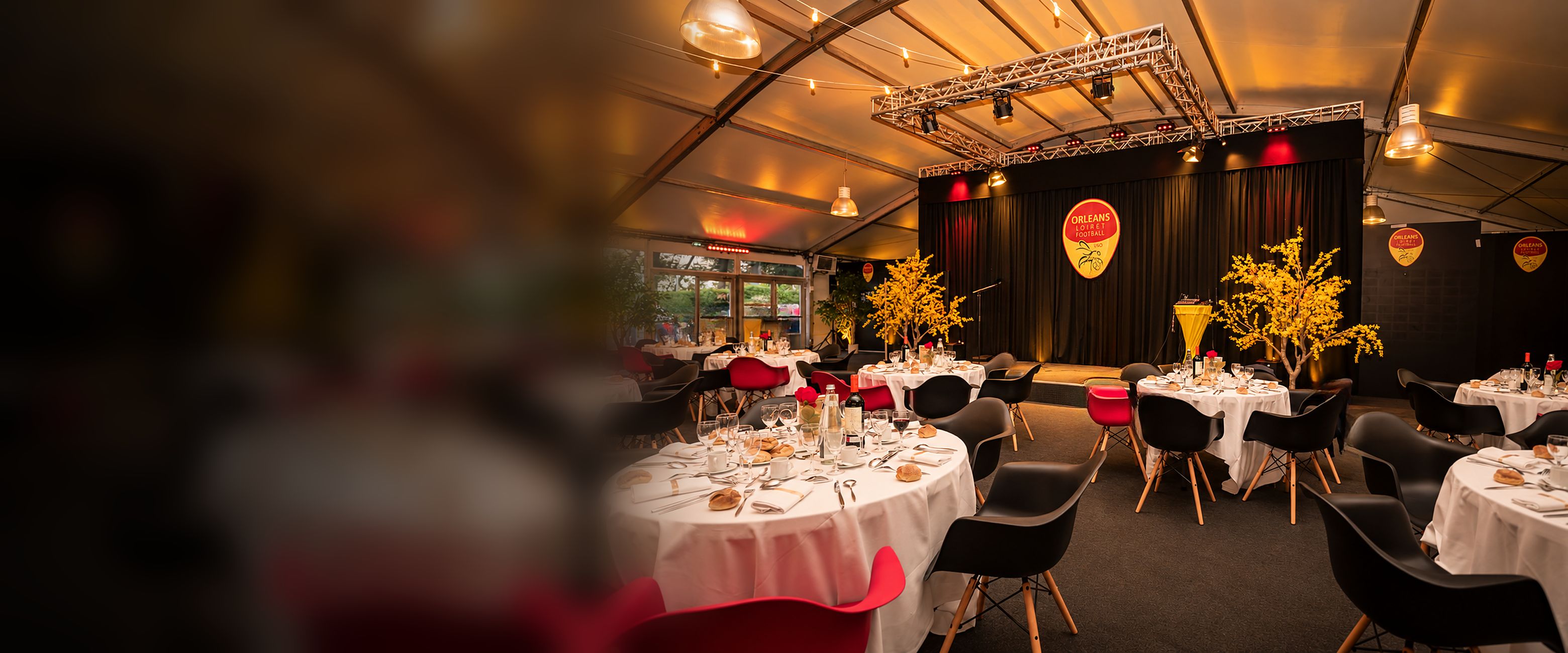 La scène de l’espace réceptif sous le logo du club, entourée de branches fleuries jaunes, face aux tables rondes dressées