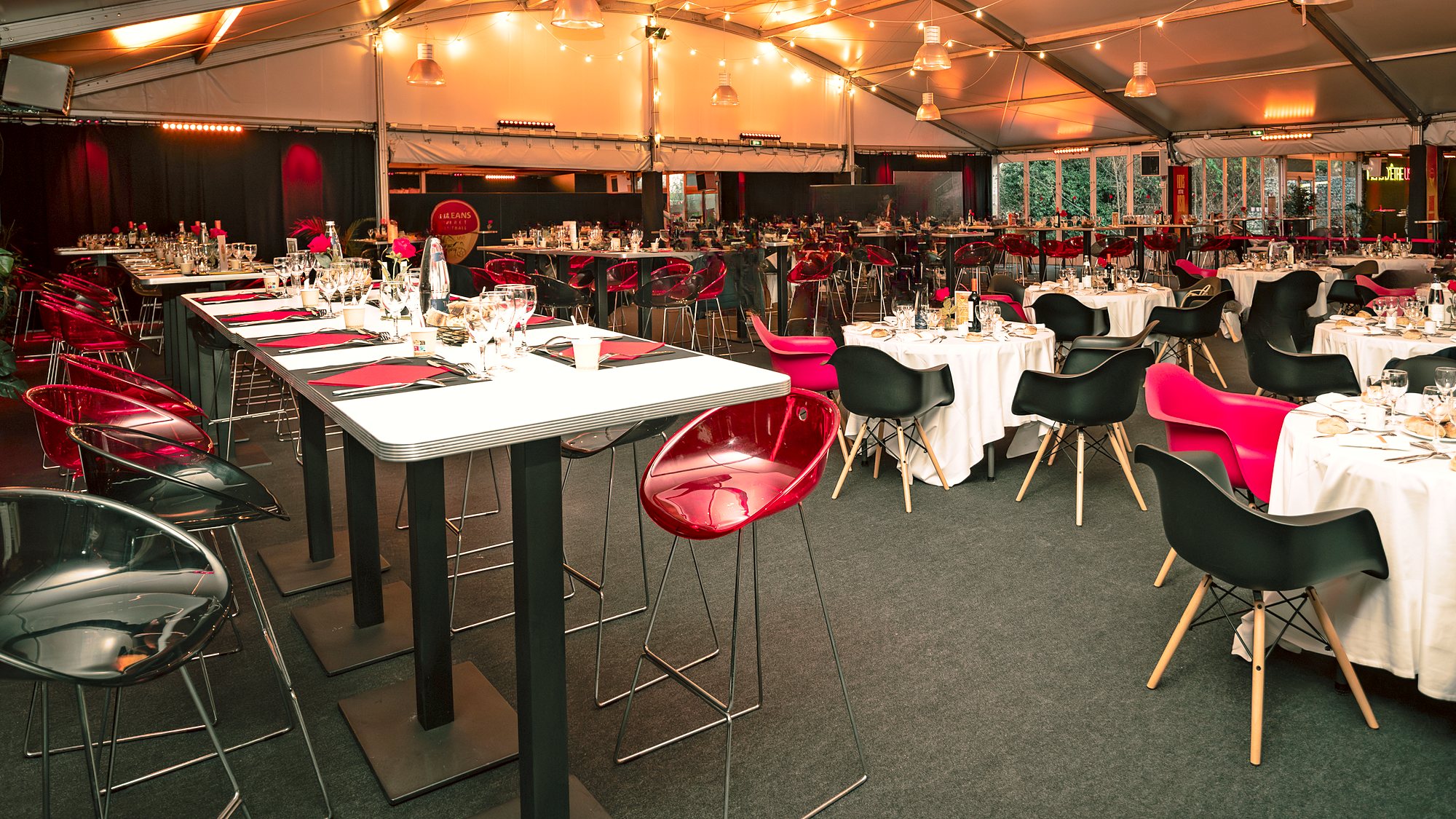 Tables hautes dressées en rouge et noir et tables rondes nappées sous les guirlandes lumineuses