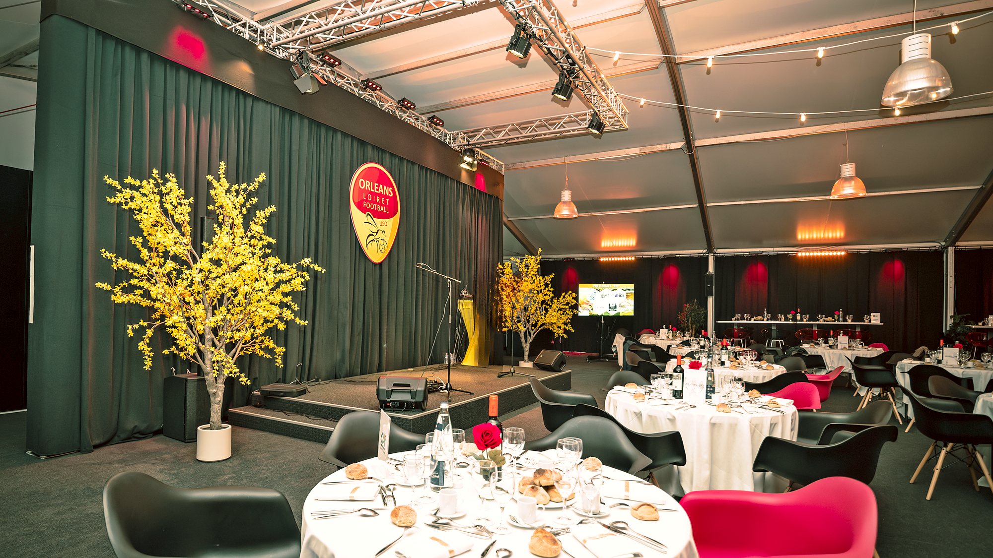 La scène sous le logo du club, entre deux arbres fleuris jaunes, face aux tables rondes dressées