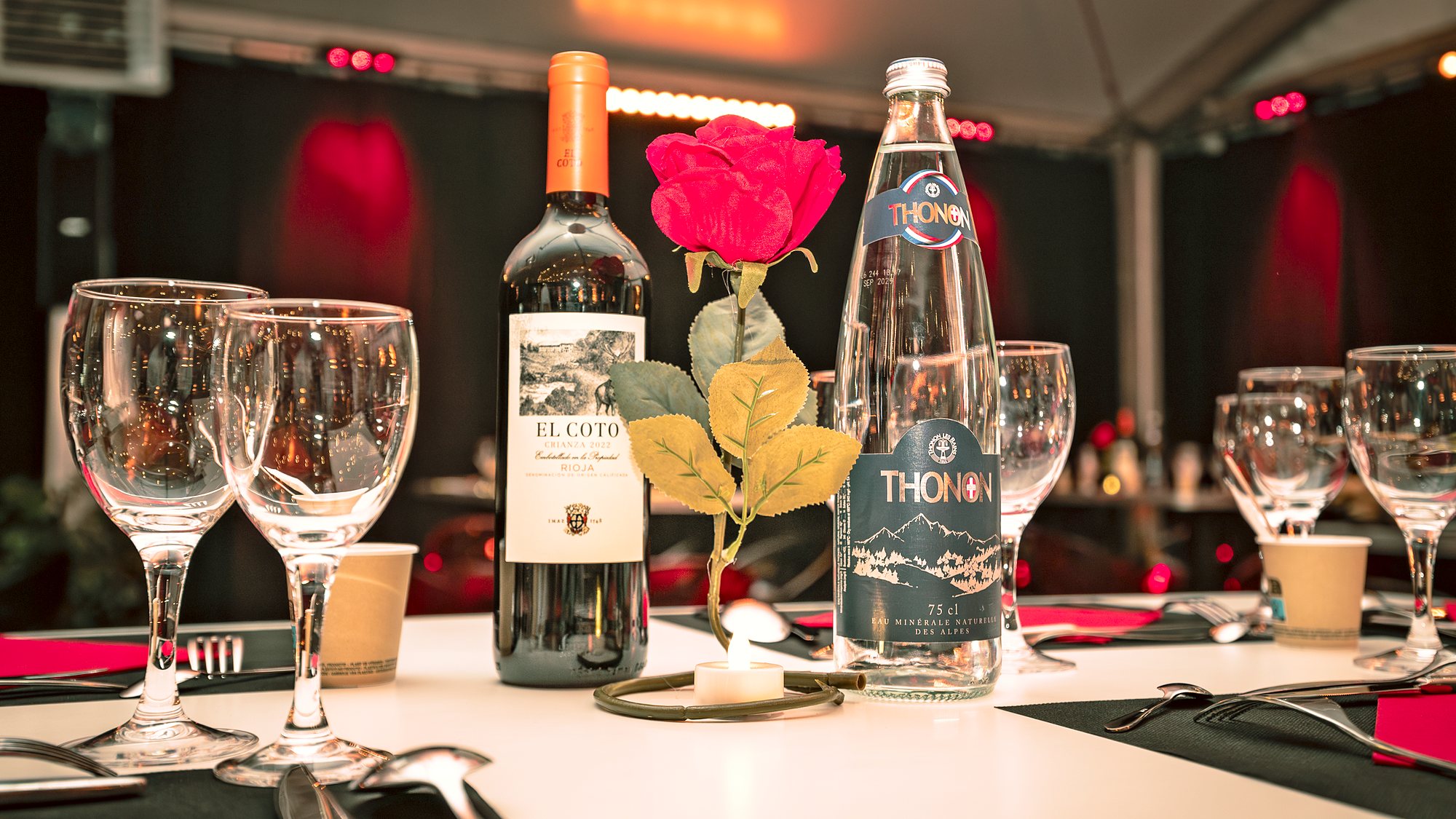 Détail d’une table dressée : verres à pied, bouteille de vin, rose rouge et bougie